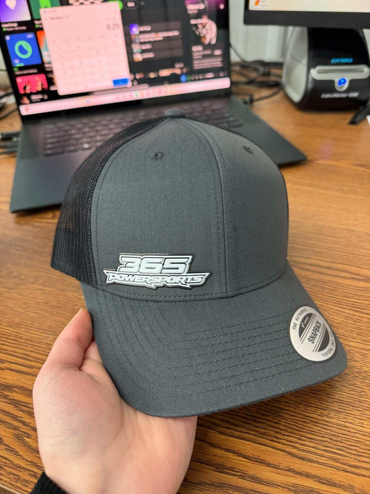 365 Retro Trucker flex patch hat in black with mesh back held over wooden desk with laptop in background