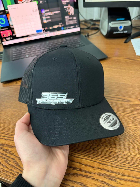 Black 365 Retro Trucker Flex Patch Hat on wooden desk.